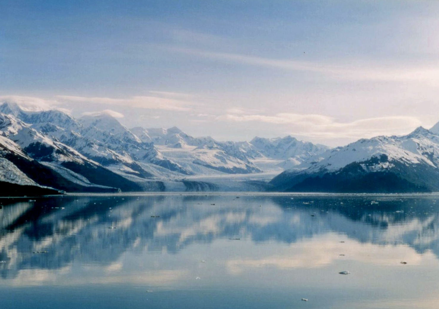 A large cruise ship sailing through a narrow Alaskan fjord with snow-capped mountains on both sides.