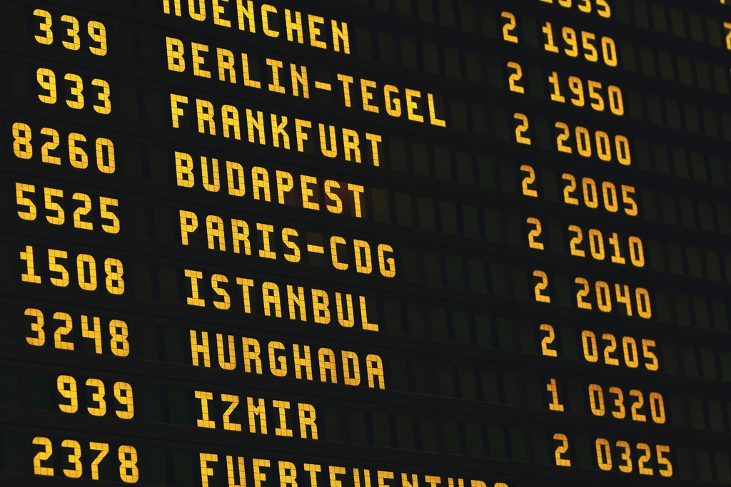 A traveler looks up at an airport departures board listing flight times and gates.