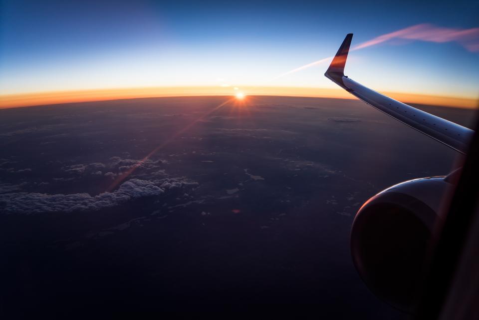 View from a passenger window of an airliner wing passing through scattered clouds.